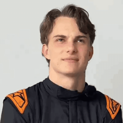 A Young Man Wearing A Racing Suit Is Smiling For The Camera . GIF