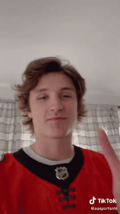 A Young Man Wearing A Red And Black Jersey With A Nhl Logo On It GIF