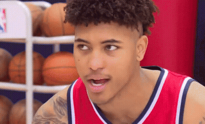 A Young Man Wearing A Red And White Basketball Jersey Is Standing In Front Of A Basketball Rack . GIF