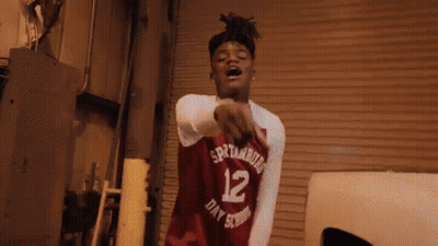 A Young Man Wearing A Red Basketball Jersey With The Number 12 On It Is Pointing At The Camera . GIF