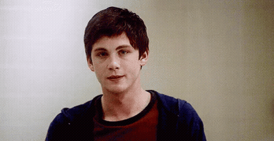 A Young Man Wearing A Red Shirt And A Blue Hoodie Is Standing In Front Of A White Wall . GIF