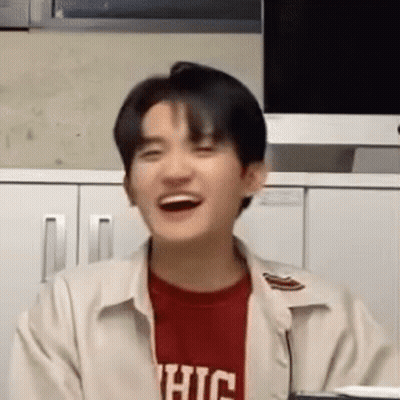 A Young Man Wearing A Red Shirt And A White Jacket Is Laughing In Front Of A Computer Monitor . GIF