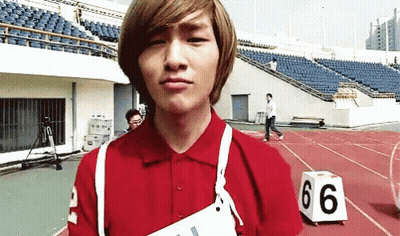 A Young Man Wearing A Red Shirt Is Standing On A Track With A Number 66 Block In Front Of Him GIF