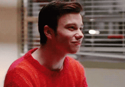 A Young Man Wearing A Red Sweater Is Smiling While Sitting In Front Of A Window . GIF