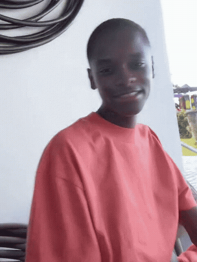 A Young Man Wearing A Red Sweatshirt Is Smiling While Sitting On A Balcony . GIF