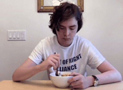 A Young Man Wearing A Shirt That Says " Of Right Alliance " Is Eating Cereal GIF
