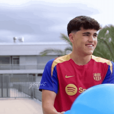 A Young Man Wearing A Spotify Shirt Smiles While Holding A Blue Ball GIF