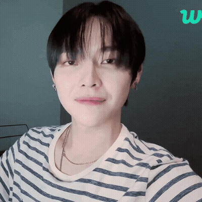 A Young Man Wearing A Striped Shirt And A Necklace Looks At The Camera GIF