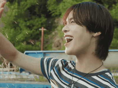 A Young Man Wearing A Striped Shirt And A Necklace With A Star On It Is Smiling GIF