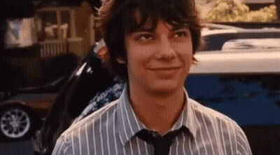 A Young Man Wearing A Striped Shirt And Tie Is Smiling While Standing In Front Of A Car . GIF