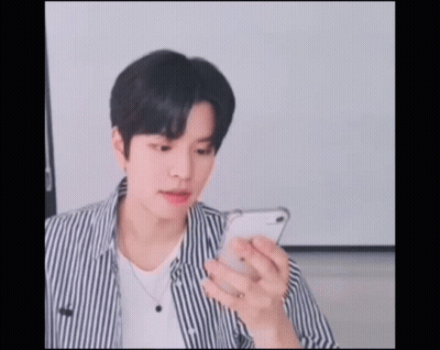 A Young Man Wearing A Striped Shirt Is Looking At His Phone GIF