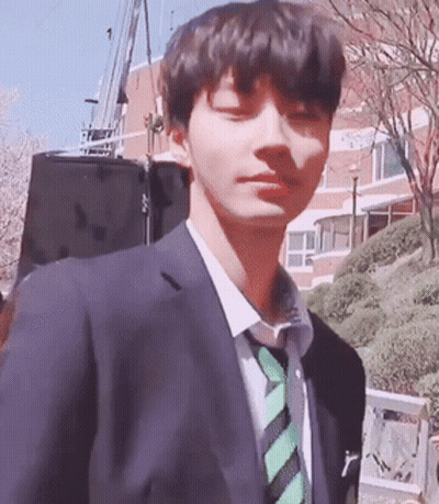 A Young Man Wearing A Suit And Tie Is Standing In Front Of A Building GIF