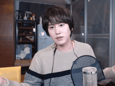 A Young Man Wearing A Sweater And Headphones Is Standing In Front Of A Microphone GIF