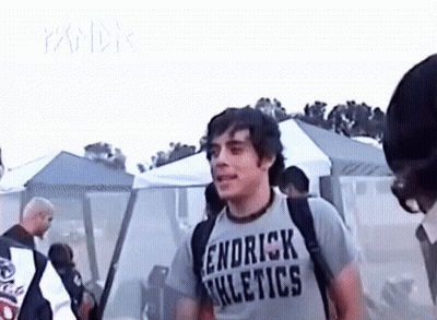 A Young Man Wearing A T-Shirt That Says Kendrick Athletics Is Standing In Front Of A Crowd Of People . GIF