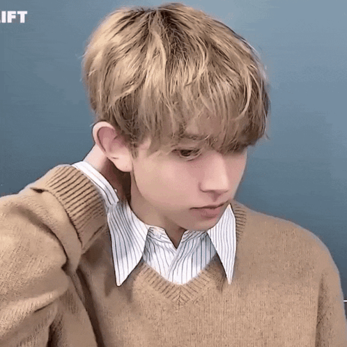 A Young Man Wearing A Tan Sweater And A Striped Shirt Has His Hand On His Neck GIF