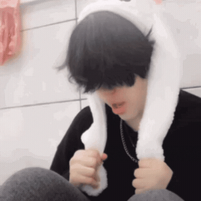 A Young Man Wearing A White Bunny Ear Hat Is Sitting Down . GIF