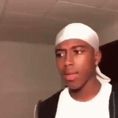 A Young Man Wearing A White Headband And A Black Jacket Is Making A Funny Face . GIF
