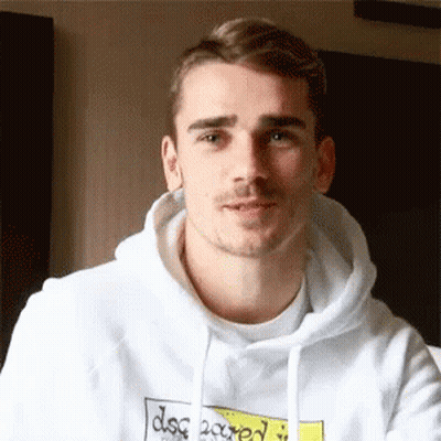 A Young Man Wearing A White Hoodie With A Yellow Sticker On It Is Looking At The Camera . GIF