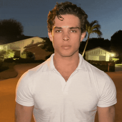 A Young Man Wearing A White Polo Shirt Is Standing In Front Of A Palm Tree GIF