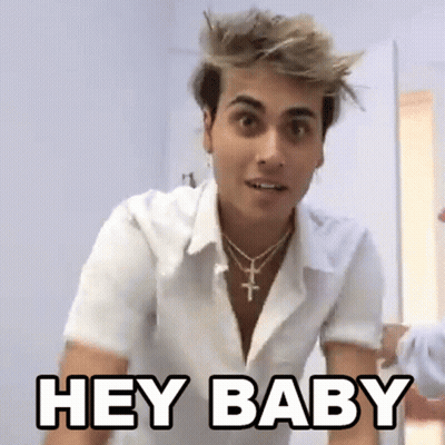 A Young Man Wearing A White Shirt And A Cross Necklace Is Standing In A Room And Saying `` Hey Baby '' . GIF