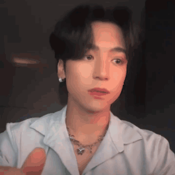A Young Man Wearing A White Shirt And A Necklace Looks At The Camera GIF