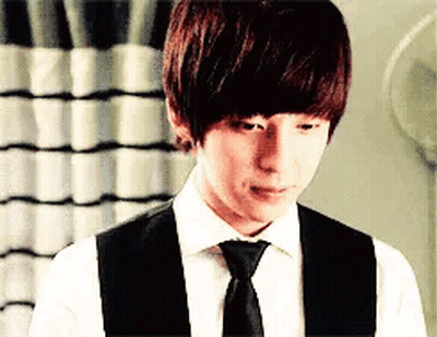 A Young Man Wearing A White Shirt And Black Vest And Tie . GIF
