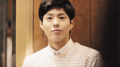 A Young Man Wearing A White Shirt And Sweater Is Looking At The Camera . GIF