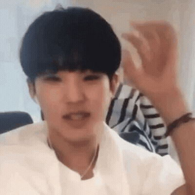 A Young Man Wearing A White Shirt Is Waving His Hand In The Air . GIF