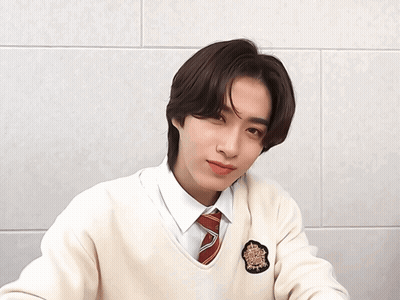A Young Man Wearing A White Sweater And A Red Tie Winks At The Camera GIF