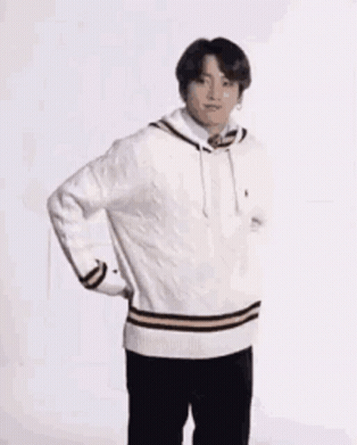 A Young Man Wearing A White Sweater And Black Pants Is Standing On One Leg . GIF