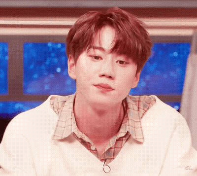 A Young Man Wearing A White Sweater And Plaid Shirt Looks To The Side GIF