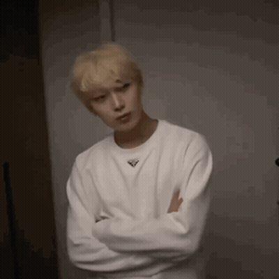 A Young Man Wearing A White Sweater With His Arms Crossed . GIF