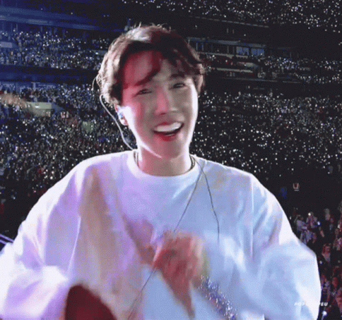 A Young Man Wearing A White Sweatshirt Is Smiling In Front Of A Crowd . GIF