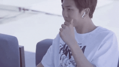 A Young Man Wearing A White T-Shirt And Ear Buds Is Sitting In A Chair . GIF