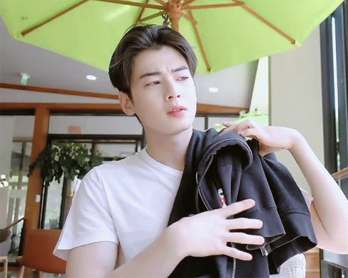 A Young Man Wearing A White T-Shirt Is Holding A Black Jacket Over His Shoulder . GIF
