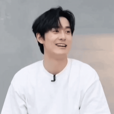 A Young Man Wearing A White T-Shirt Is Smiling And Looking At The Camera . GIF