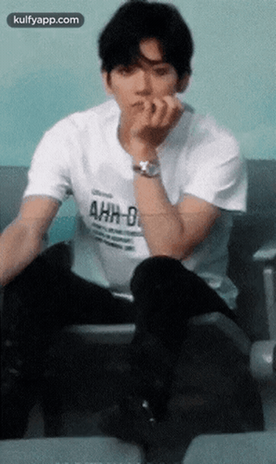 A Young Man Wearing A White T-Shirt That Says Ahh-D Is Sitting On A Chair GIF