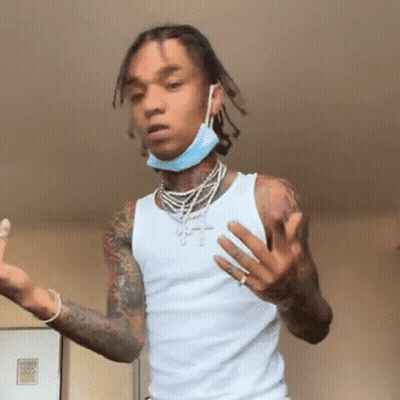 A Young Man Wearing A White Tank Top And A Blue Face Mask Is Standing In A Room . GIF