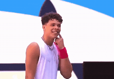 A Young Man Wearing A White Tank Top And A Pink Wristband Smiles GIF