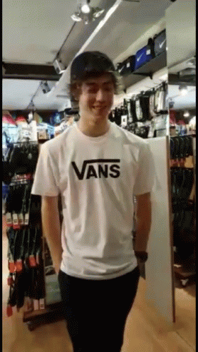 A Young Man Wearing A White Vans T-Shirt Stands In A Store GIF