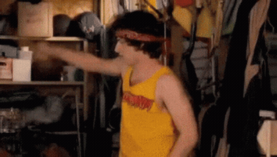 A Young Man Wearing A Yellow Tank Top And A Bandana Is Standing In A Closet . GIF