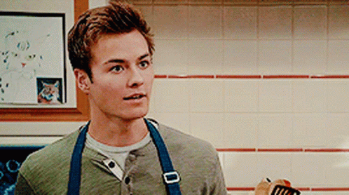 A Young Man Wearing An Apron Is Holding A Spatula GIF