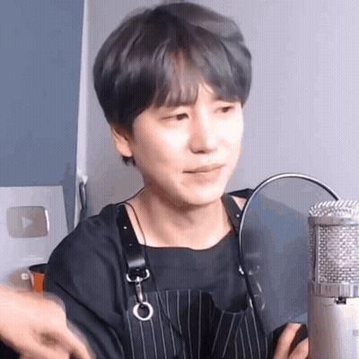 A Young Man Wearing An Apron Is Sitting In Front Of A Microphone And Making A Funny Face . GIF