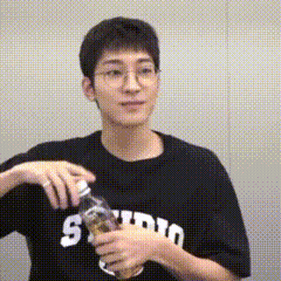A Young Man Wearing Glasses And A Black T-Shirt Is Holding A Bottle Of Water . GIF