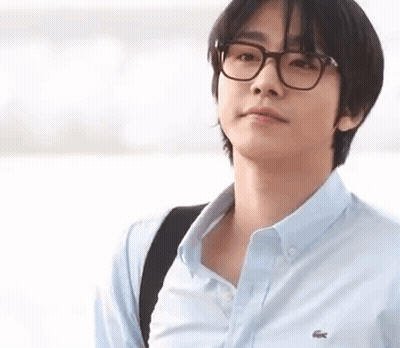 A Young Man Wearing Glasses And A Blue Shirt Is Standing In Front Of A Body Of Water . GIF