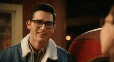 A Young Man Wearing Glasses And A Denim Jacket Is Smiling . GIF