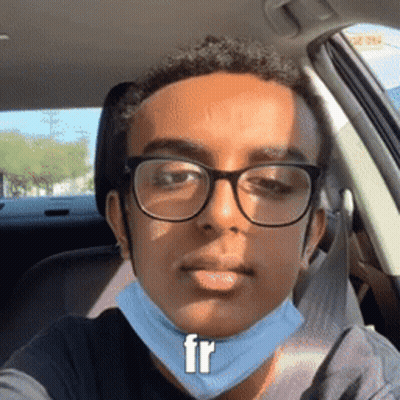A Young Man Wearing Glasses And A Face Mask Is Sitting In A Car GIF