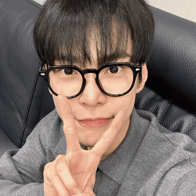 A Young Man Wearing Glasses And A Grey Shirt Giving A Peace Sign GIF