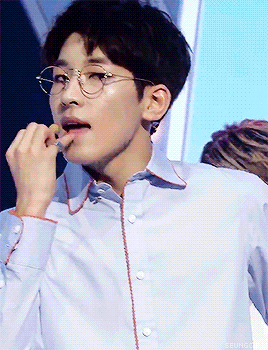 A Young Man Wearing Glasses And A Light Blue Shirt Is Eating Something GIF