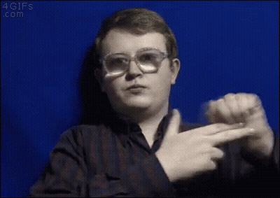 A Young Man Wearing Glasses And A Plaid Shirt Is Pointing At The Camera . GIF